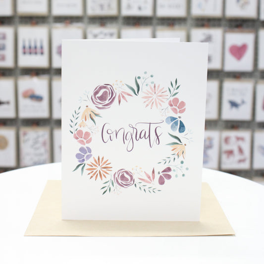 Hand crafted greeting card with watercolor spring flowers circling Congrats.