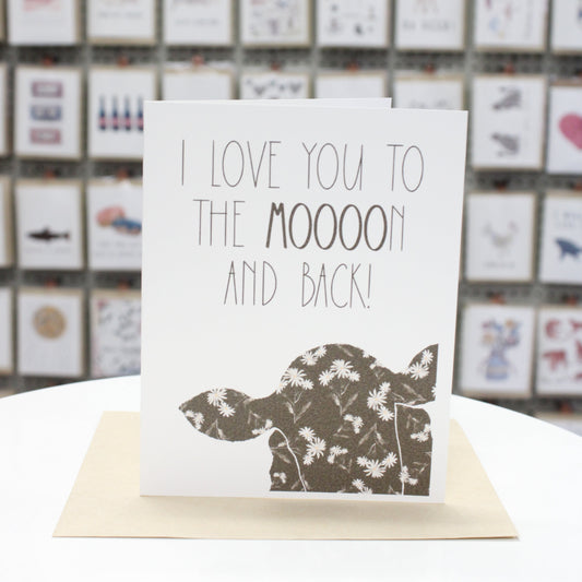 Hand crafted greeting card with printed cow head and flowers inside. Written in large letters, "I Love You To The Moooon And Back!"