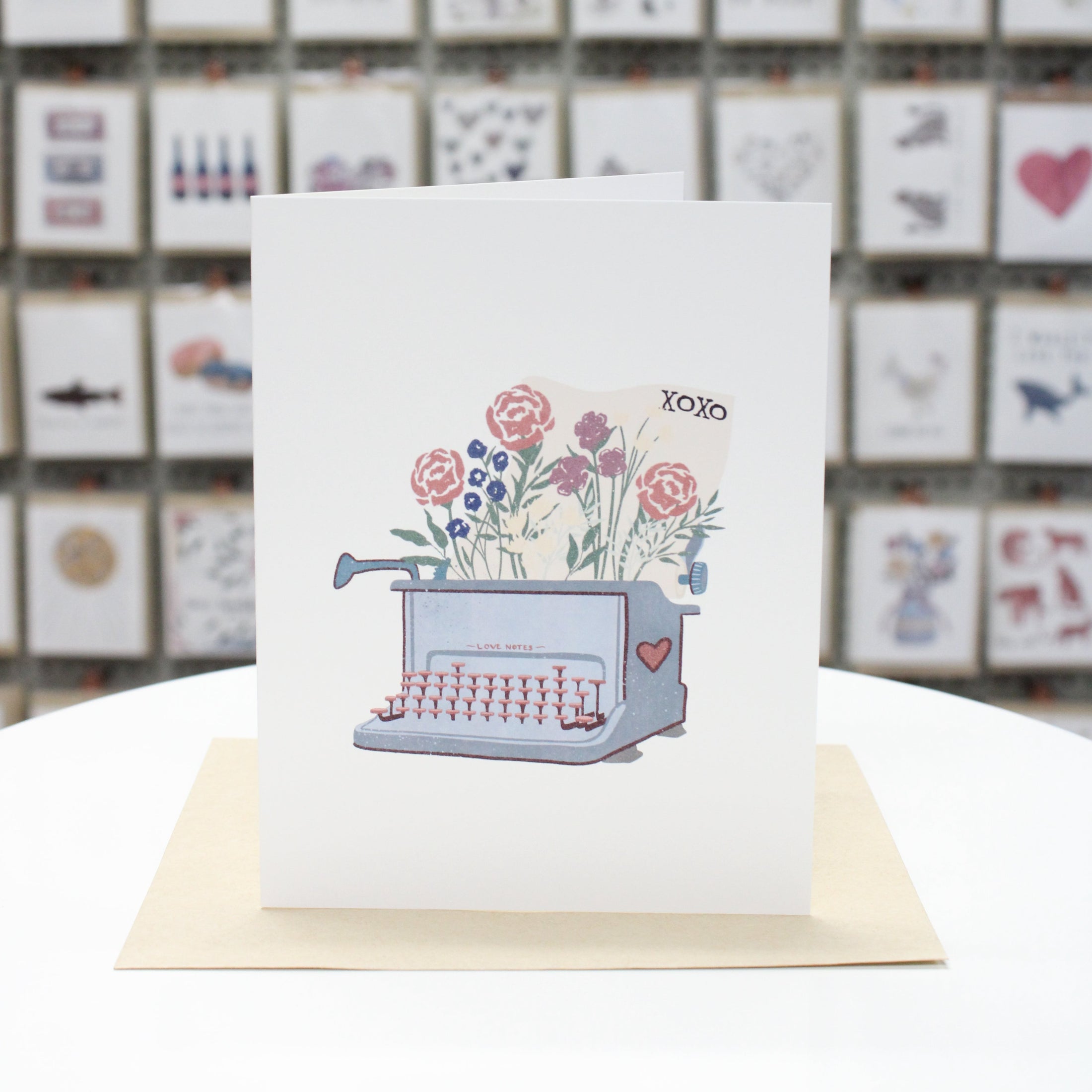 Handcrafted greeting card with typewriter with stenciled flower paper feeding through. The letters "XOXO" on top corner of paper.  