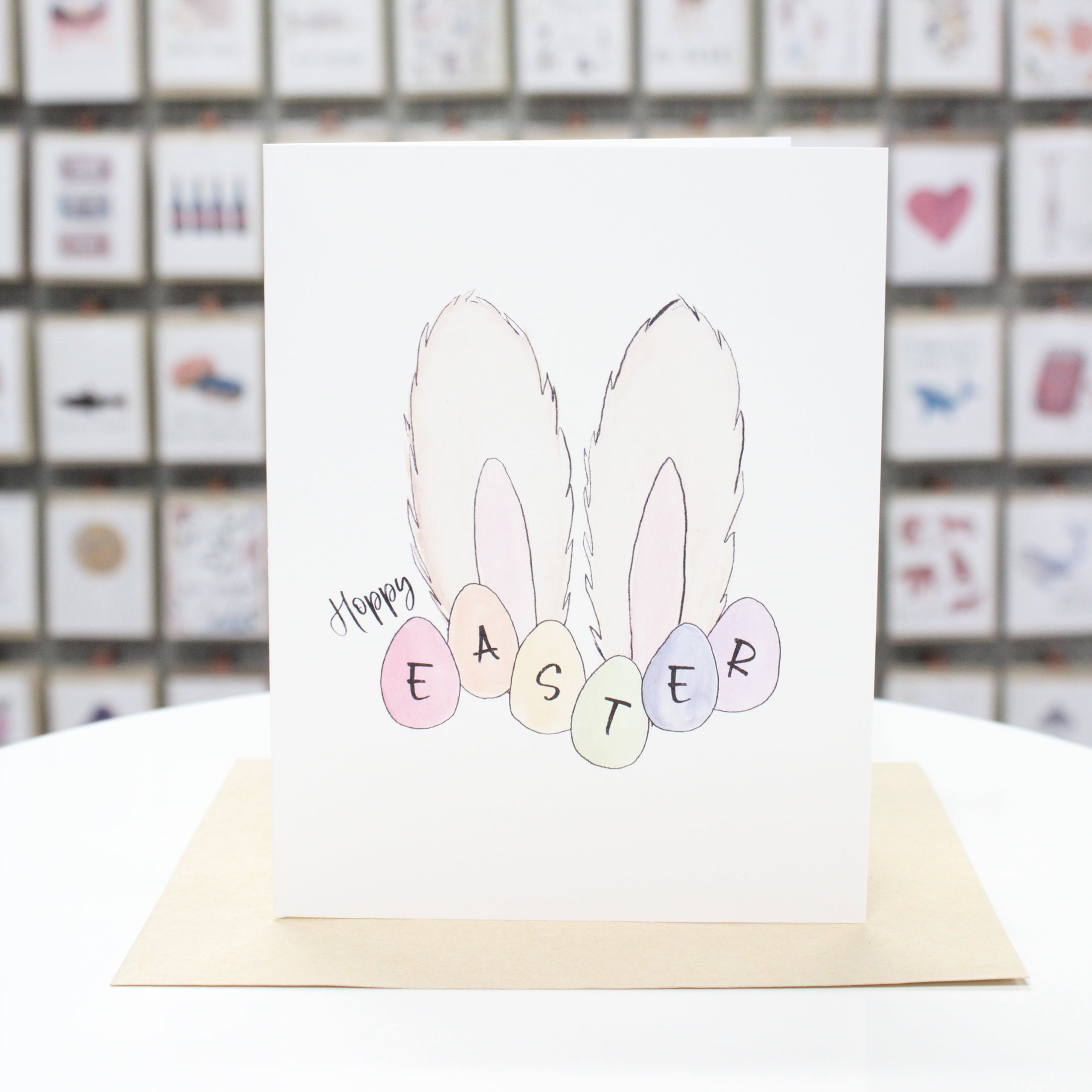 Hand crafted greeting card with fluffy bunny ears and eggs at the base. Card reads, "Hoppy Easter" with the word Easter inside the eggs. 