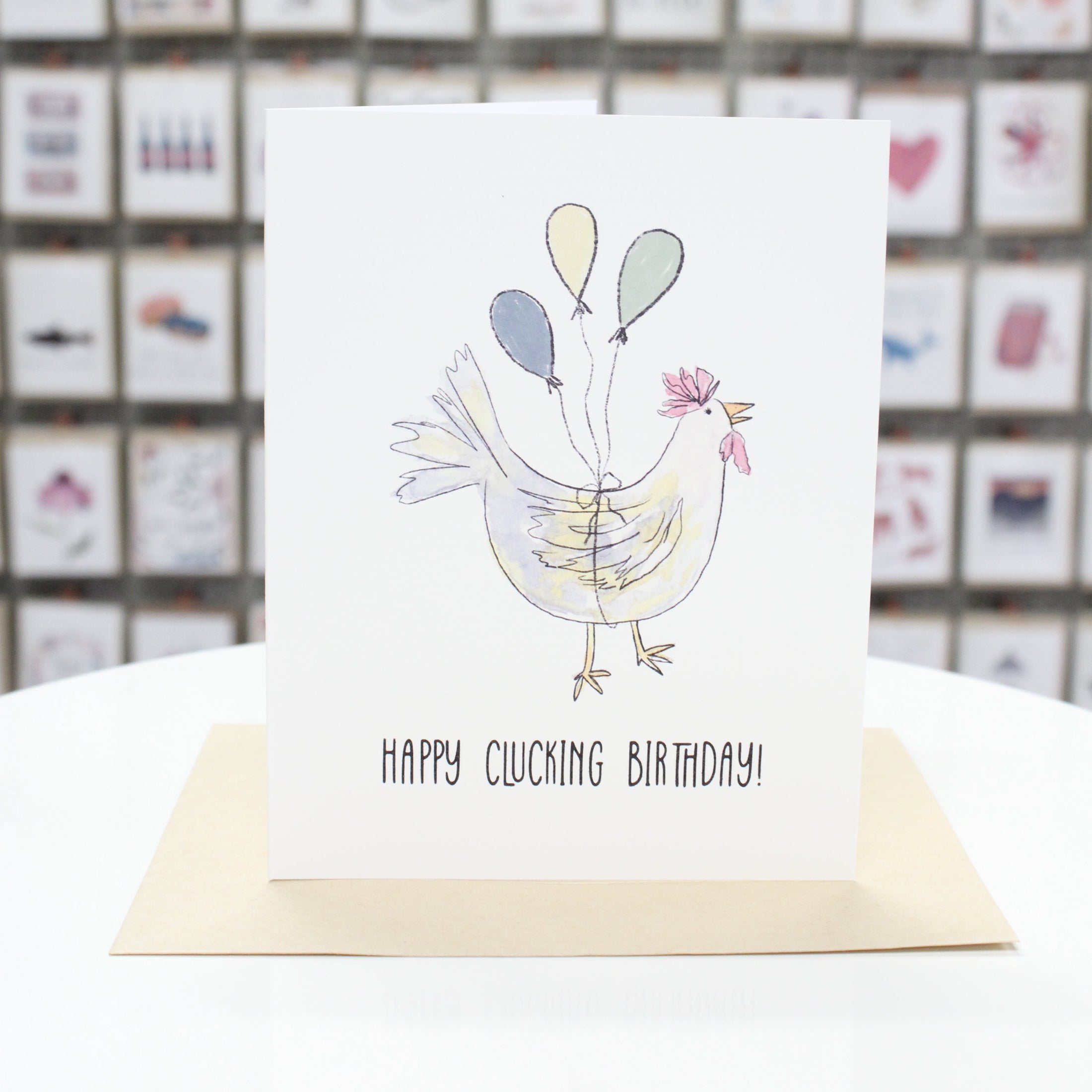 Hand crafted greeting card with hand drawn chicken and balloons tied around the chicken's middle. Card stating, "Happy Clucking Birthday" at the bottom. 